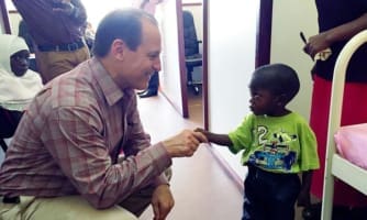 Russell E. Ware M.D., Ph.D., shaking hands with a young sickle cell patient in Africa.